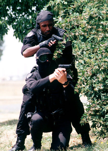 SRA Dave Orth (L) and SRA Clarence Tolliver (R), members of the 60th Security Police Squadron's Base Swat Team, Travis Air Force Base wearing black uniforms stand with M-9 pistols ready behind covering foliage. They are participating in a simulated hostage (Released to Public) (Photo credit: Wikipedia)