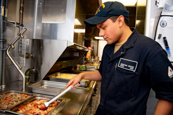 SOUTH CHINA SEA (Oct. 31, 2019) Culinary Specialist Seaman Apprentice Cristian Reyes, from Hanover Park, Ill., prepares food in the galley aboard Independence-variant littoral combat ship USS Gabrielle Giffords (LCS 10). Gabrielle Giffords is on a rotational deployment to INDOPACOM, conducting operations, exercises and port visits throughout the region and working hull-to-hull with allied and partner navies to provide maritime security and stability, key pillars of a free and open Indo-Pacific. (U.S. Navy photo by Mass Communication Specialist 3rd Class Josiah J. Kunkle/Released)